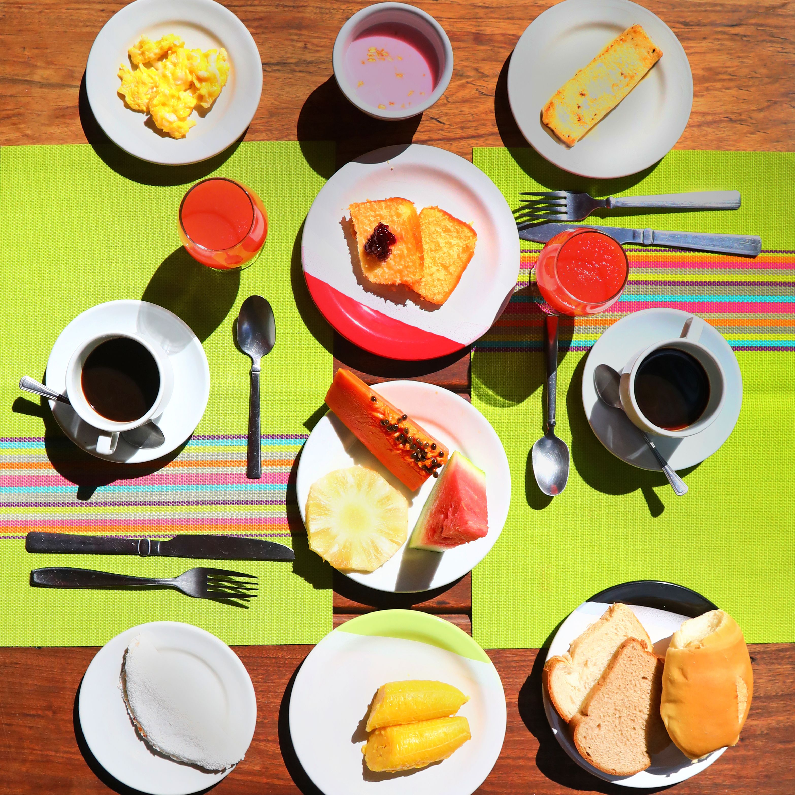 A table set with breakfast items including scrambled eggs, pancakes, toast, fruit, and beverages.
