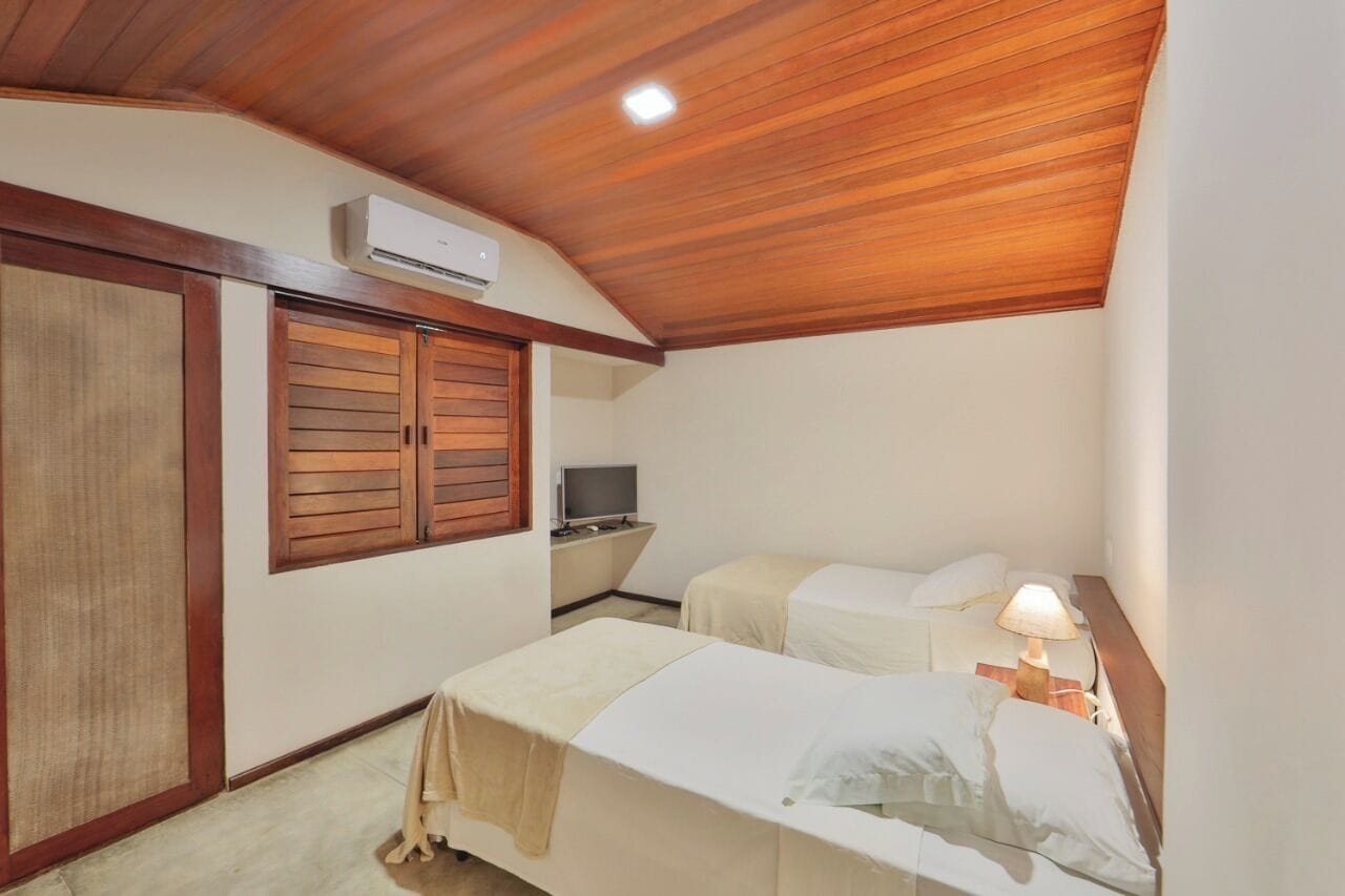 A small hotel room with two beds, a TV, and an air conditioning unit.