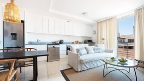 Una cocina moderna con armarios blancos, un comedor con mesa y sillas de madera, un sofá y un pequeño balcón con vistas.
