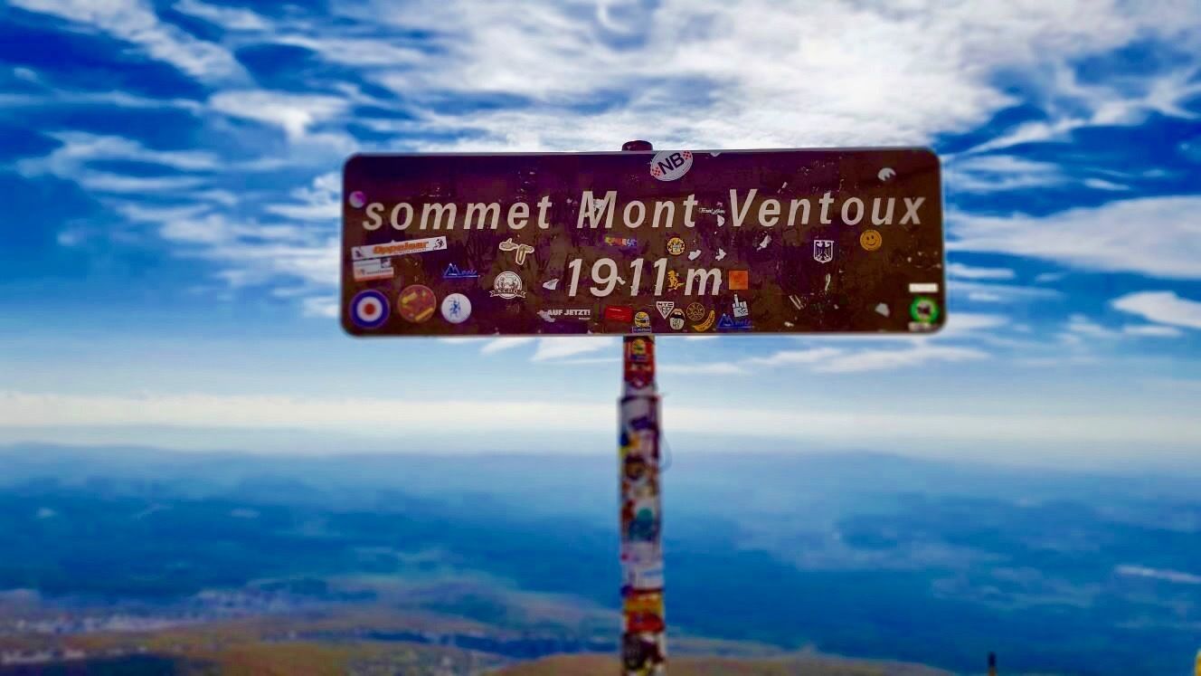 Un cartel con el texto 'Sommet Mont-Ventoux 1911m' y varias pegatinas.