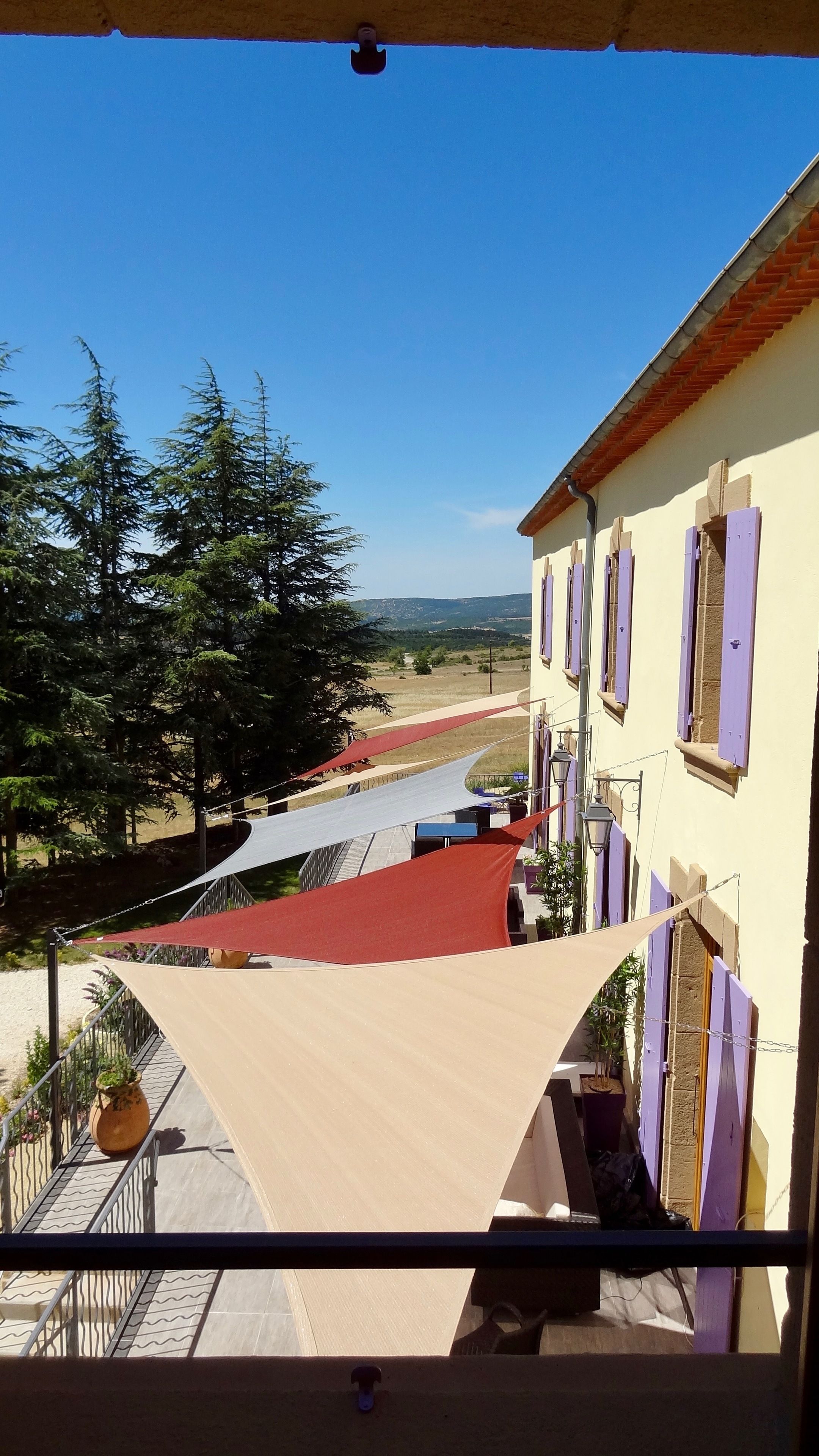 A balcony with a view of a building with purple shutters, a red pathway, and trees.