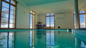 An indoor swimming pool with clear blue water, large windows, and a table with chairs. - Résidence Château Ferrassières (Ferrassières)