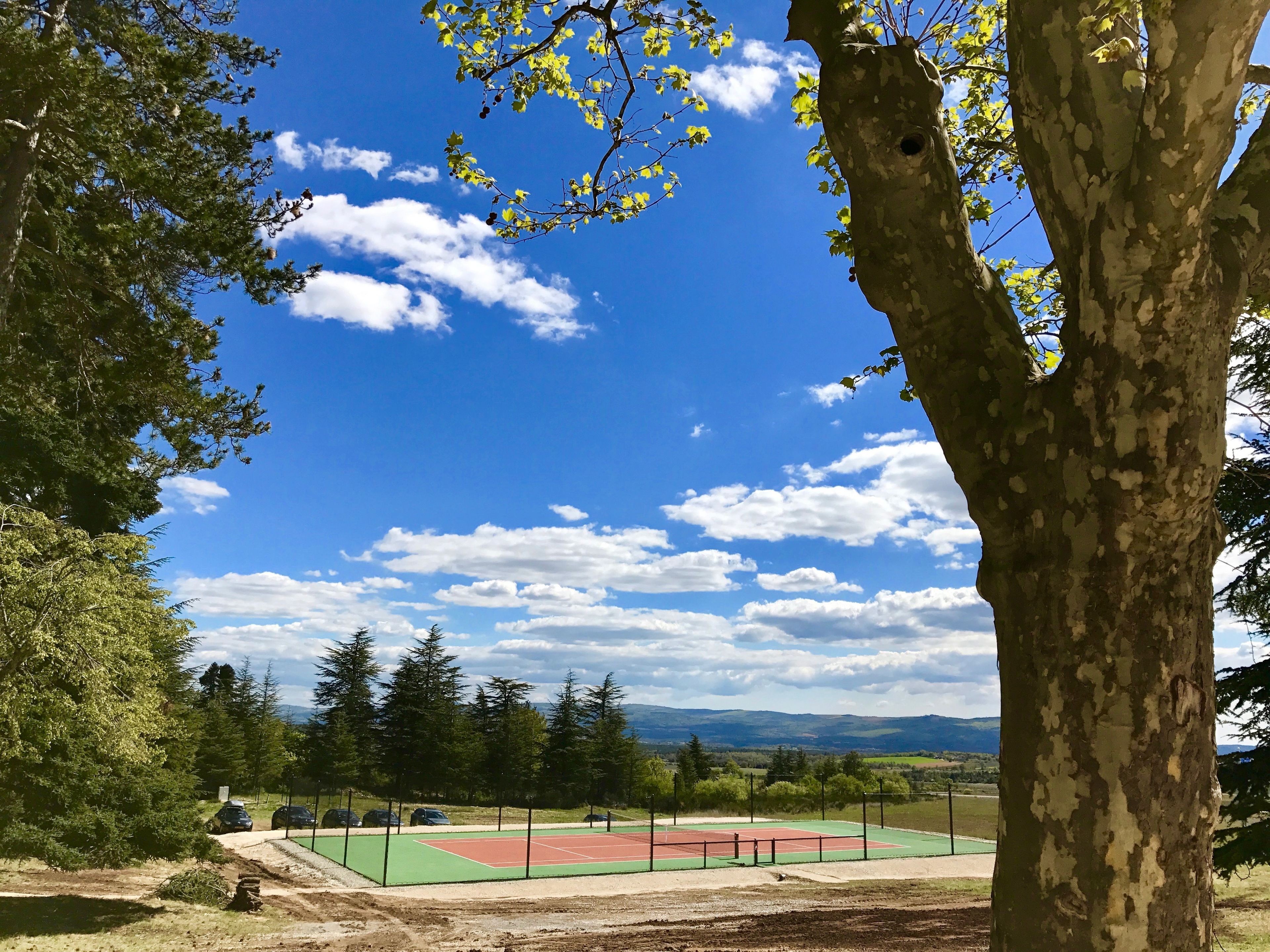 A tennis court surrounded by trees and a clear sky.