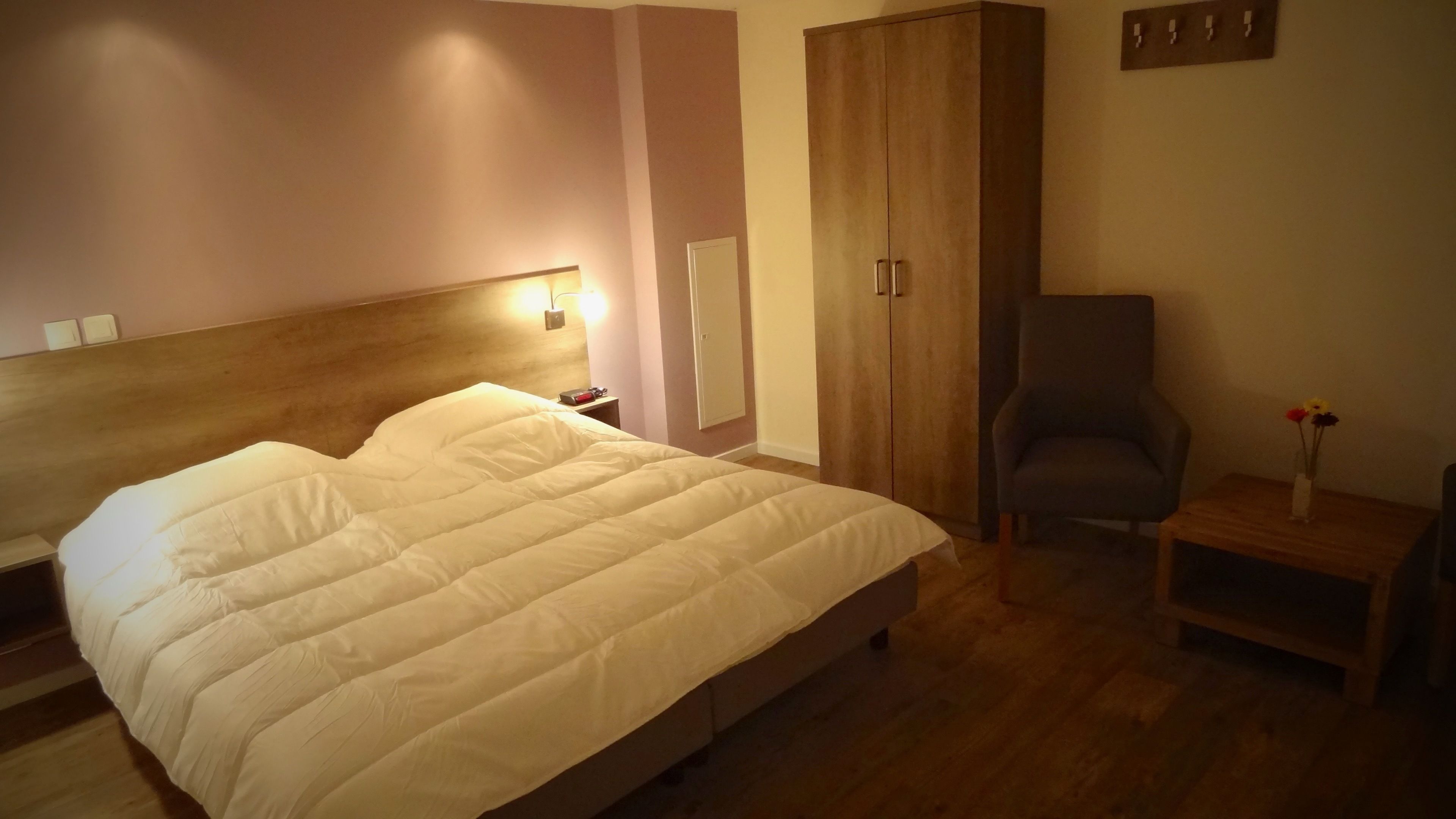Une chambre à coucher avec un grand lit, une armoire, une chaise et une petite table sur laquelle se trouve un vase.