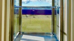 A hotel entrance with a glass door leading to a balcony with a clear view of a beach and sky. - Résidence Château Ferrassières (Ferrassières)