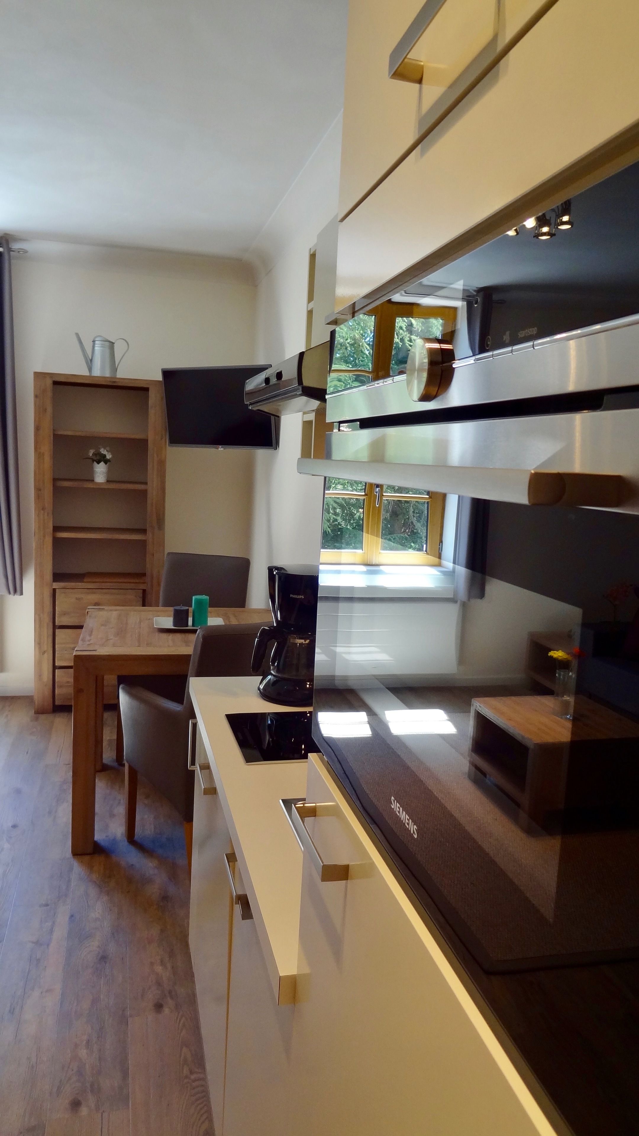 A modern kitchen with a built-in stove, a coffee maker, and a window with a view of greenery.
