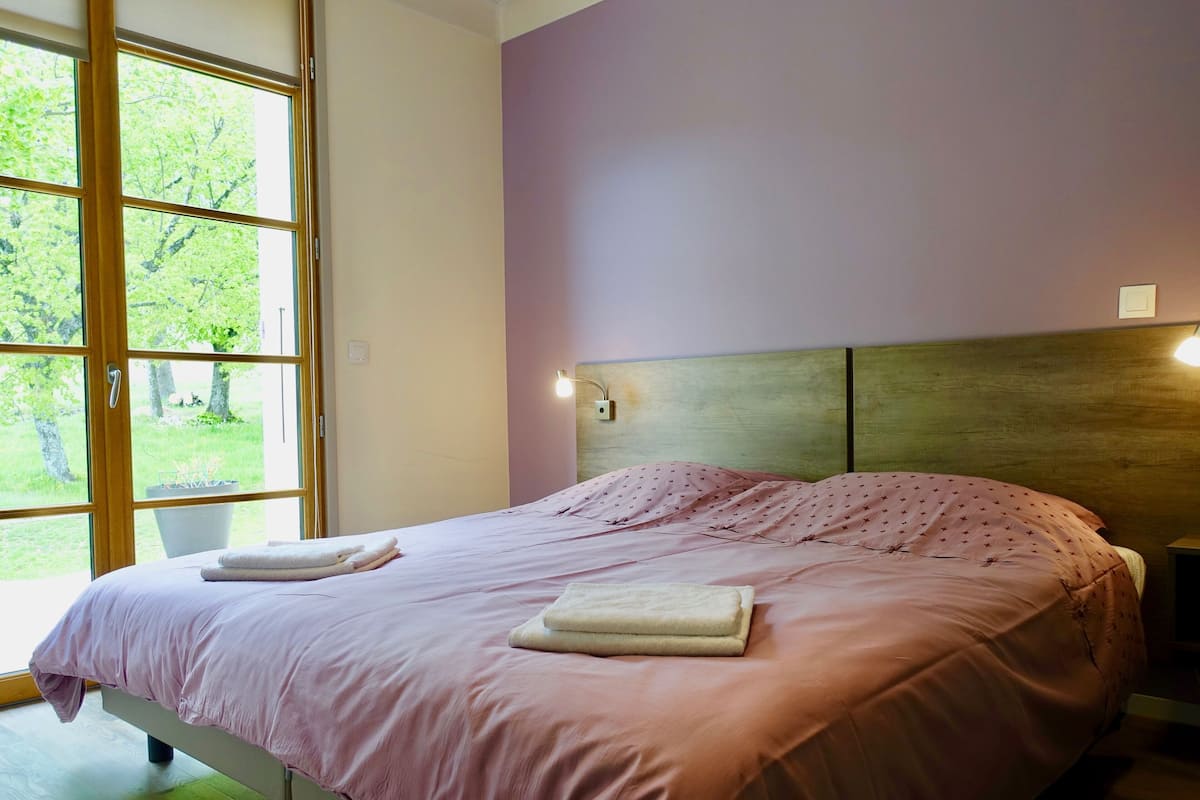 Un dormitorio con cama, mesita de noche y ventana con vistas a árboles.