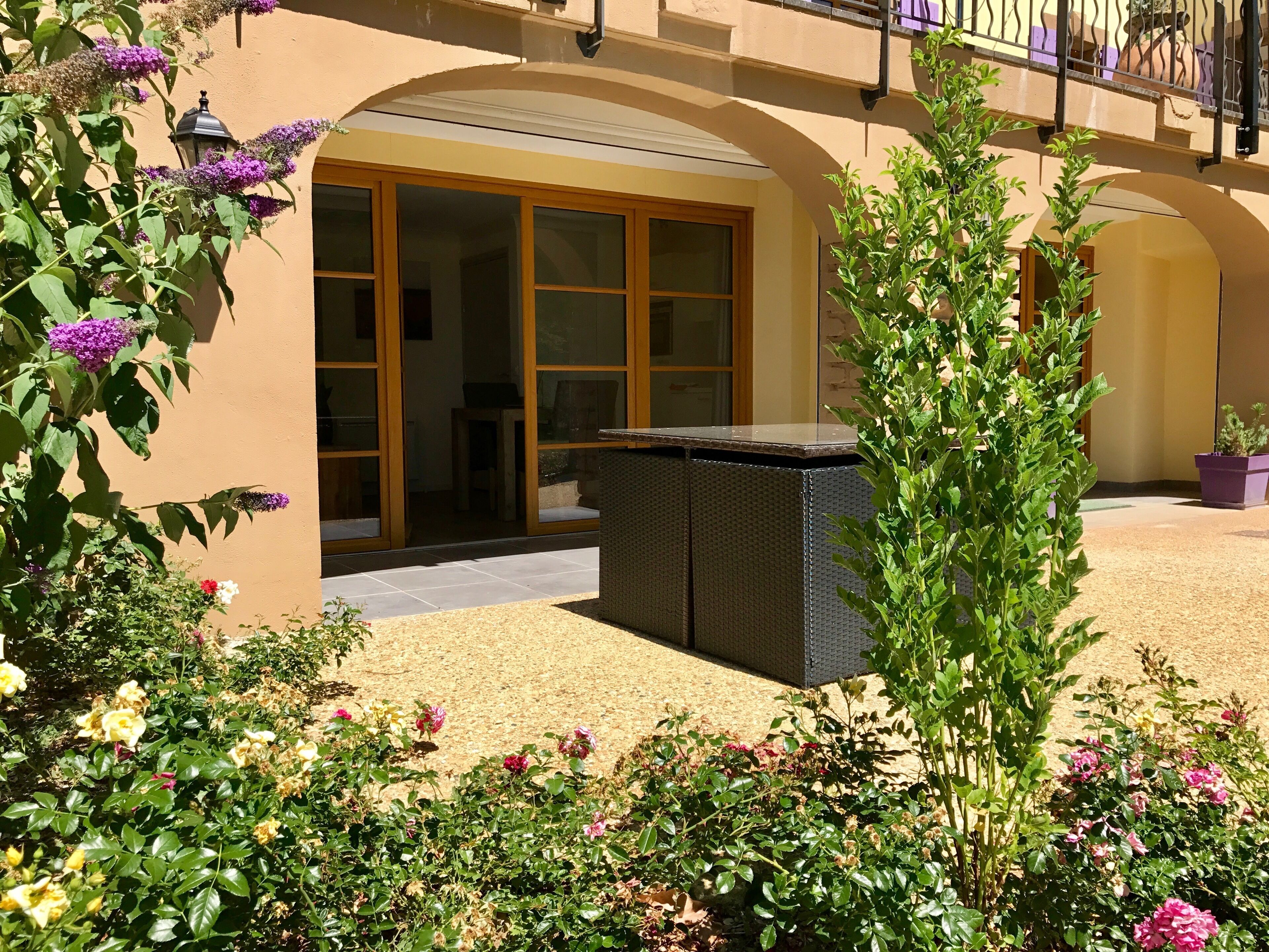 Un patio con un conjunto de asientos, una pérgola y diversas plantas en flor.