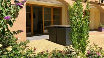 Un patio con un conjunto de asientos, una pérgola y diversas plantas en flor.