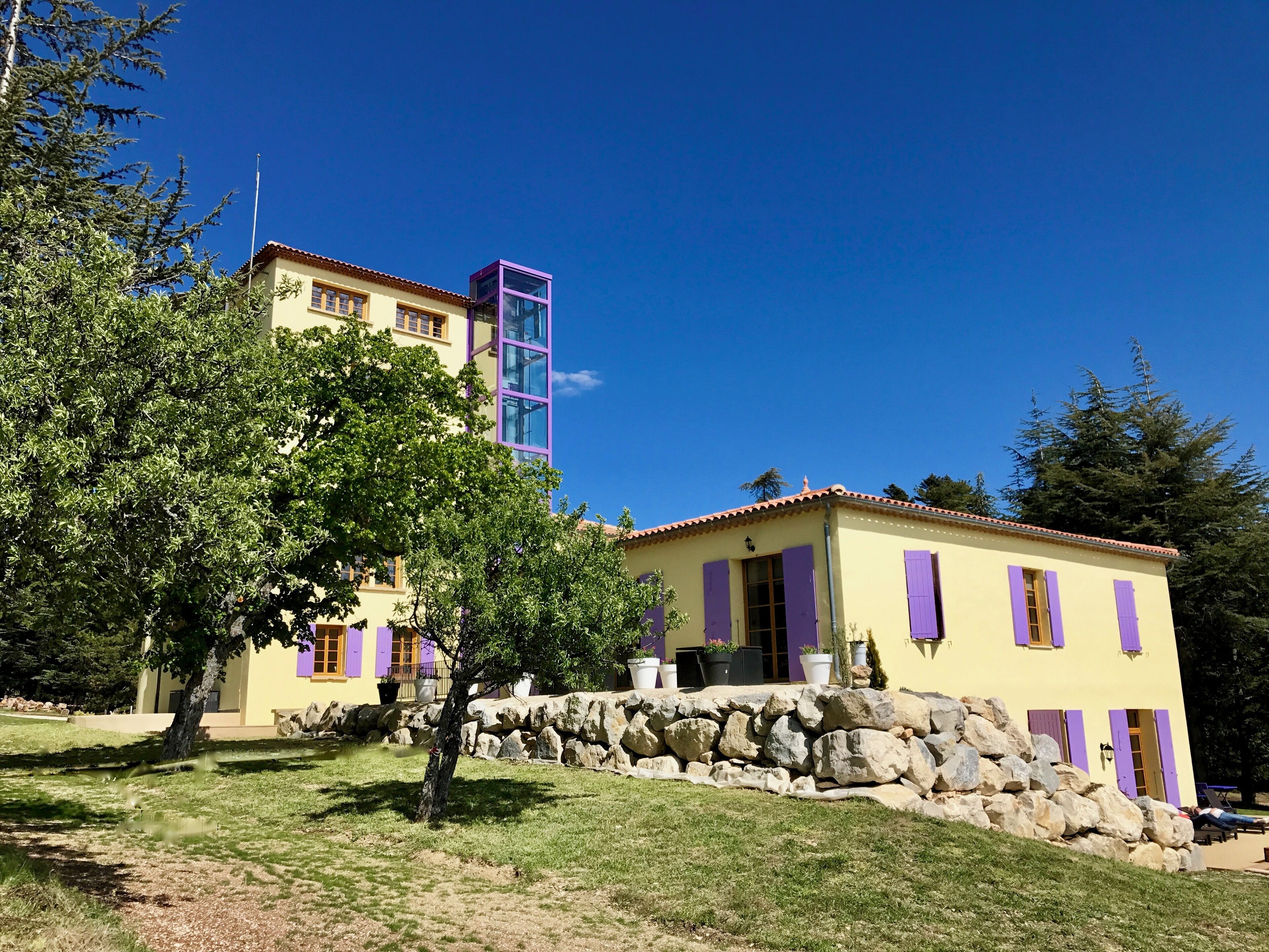 Ein gelbes Gebäude mit violetten Fensterläden und einer Mauer davor.