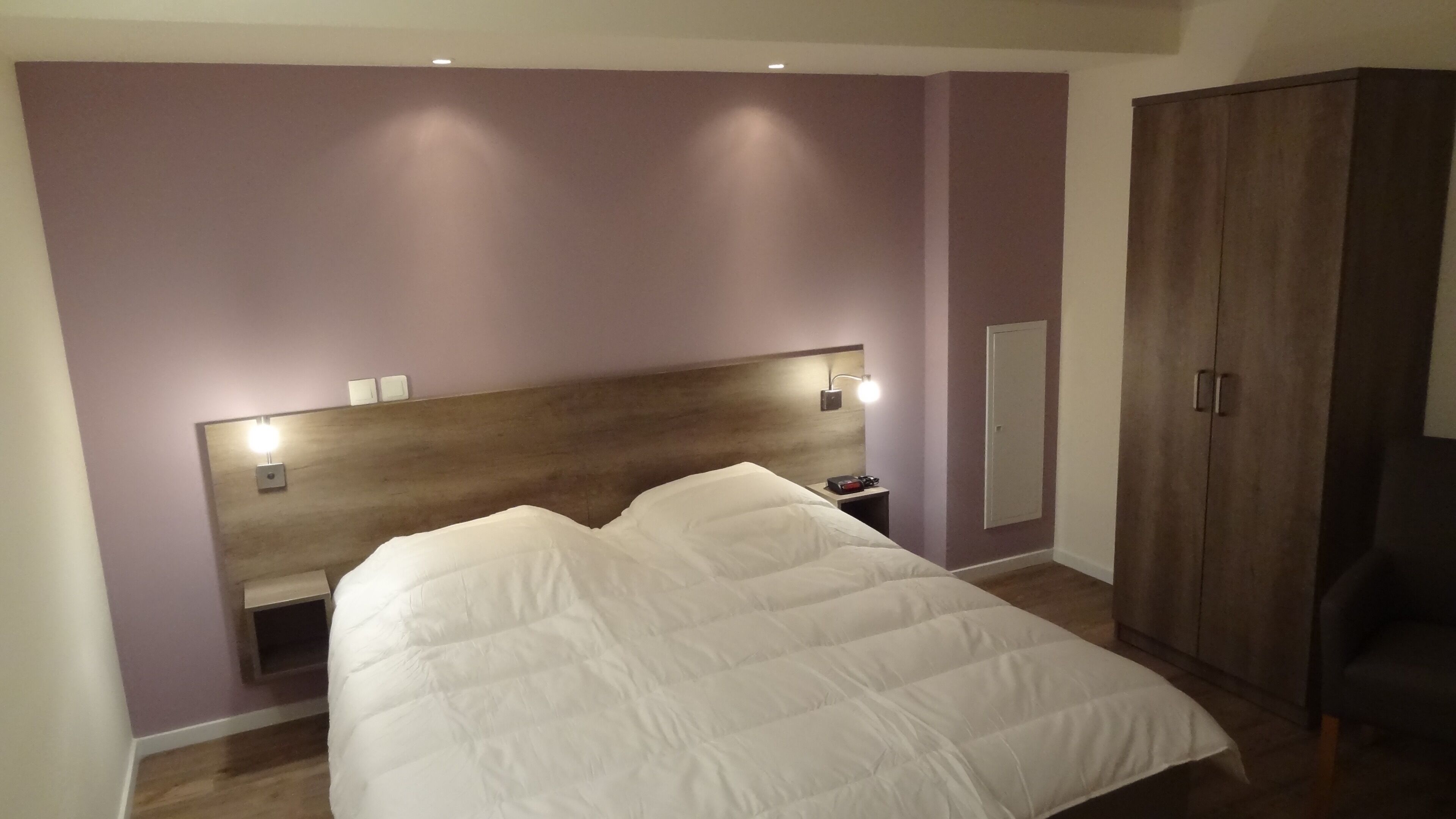 Une chambre à coucher comprenant un lit, une table de chevet, une commode, une armoire et des lampes fixées au mur.