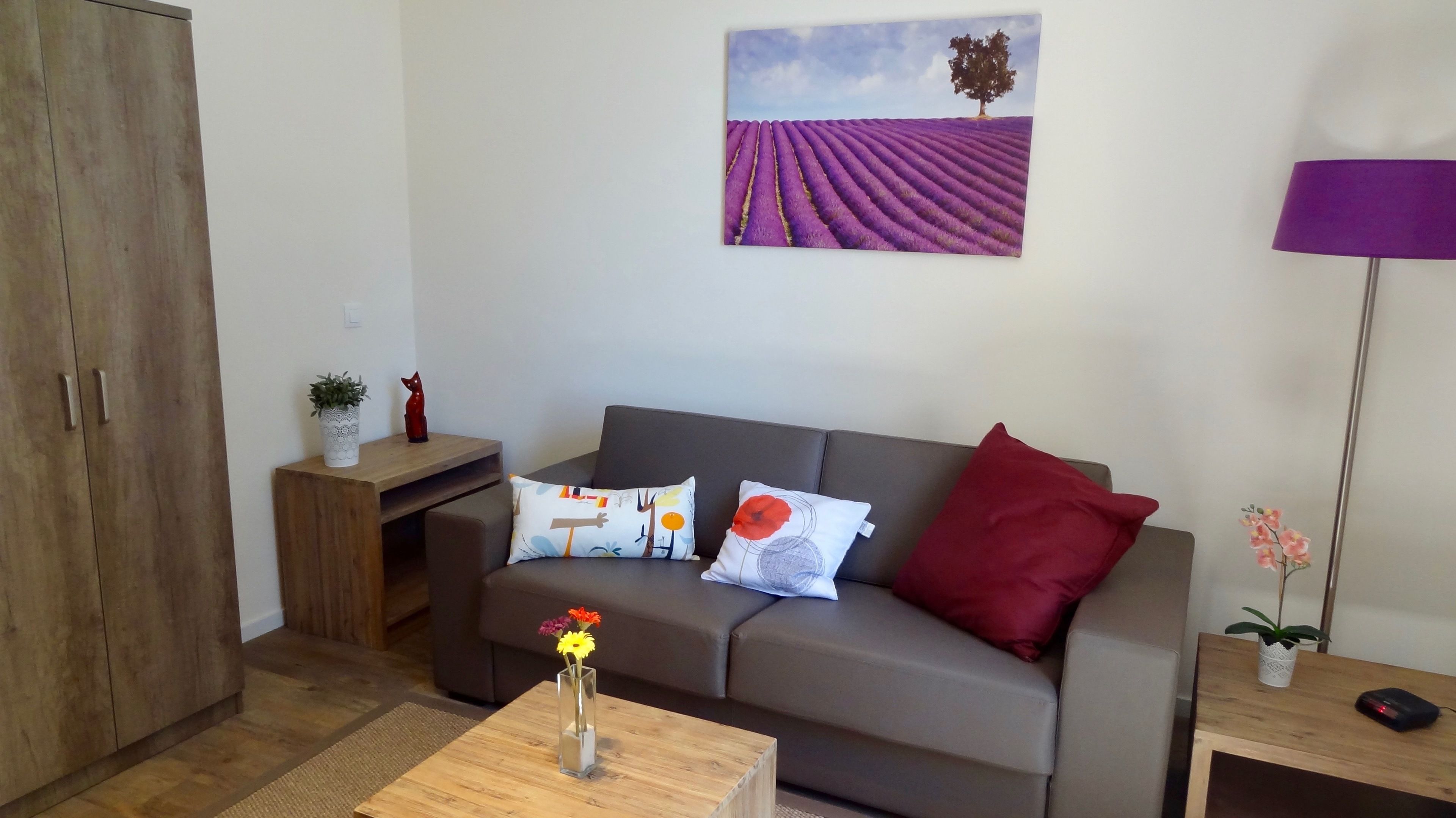 A living room with a grey sofa, a wooden coffee table, and a painting of a lavender field.