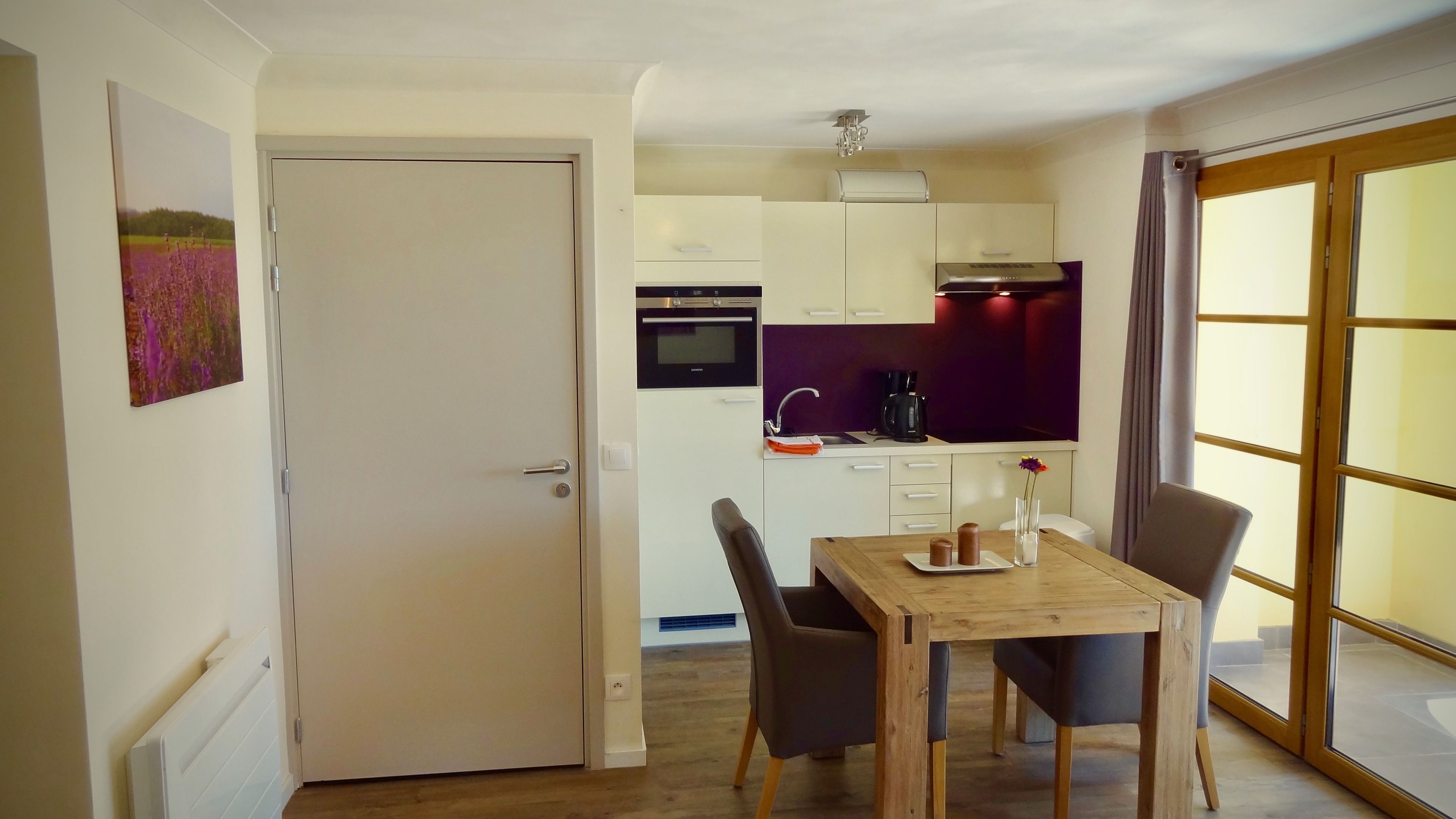 Une cuisine compacte dotée d’appareils électroménagers modernes, un coin repas avec une table et des chaises en bois, et une vue à travers une porte vitrée.