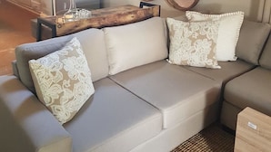 Un salon avec un canapé d’angle beige, deux coussins décoratifs à motifs, une table basse en bois et trois miroirs fixés au mur.