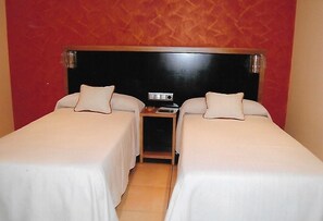 Ein Hotelzimmer mit zwei Einzelbetten, einem Holzkopfteil, einem kleinen Nachttisch und einer roten Akzentwand.
