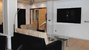 Ein modernes Hotelzimmer mit einer Couch, einem Glastisch, einem an der Wand montierten Fernseher und einem großen Fenster.