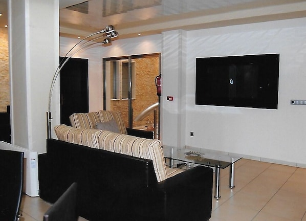 Une chambre d’hôtel moderne avec un canapé, une table en verre, un téléviseur fixé au mur et une grande fenêtre.