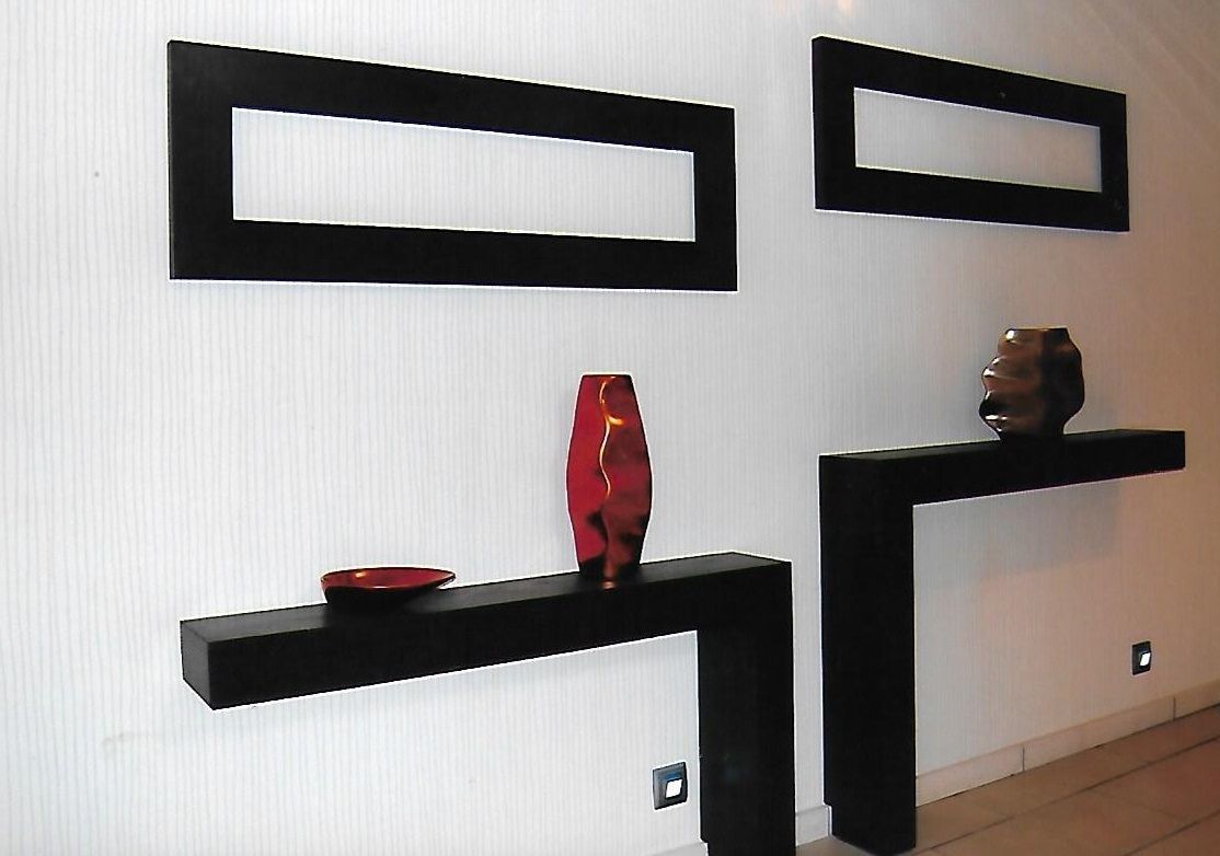 Un interior moderno con estantes negros sobre una pared blanca, cada uno exhibiendo un único objeto decorativo.