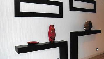 Un interior moderno con estantes negros sobre una pared blanca, cada uno exhibiendo un único objeto decorativo.