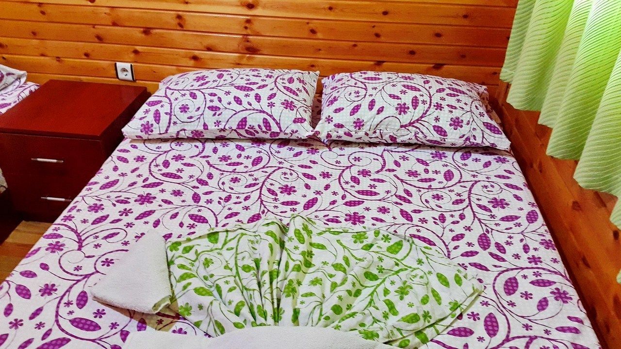 A bed with patterned bedding, a wooden headboard, and a green curtain.