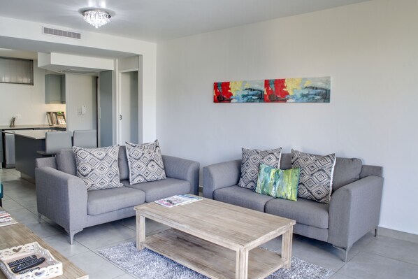 A modern living room with a grey sofa set, a wooden coffee table, and a colorful abstract painting on the wall.