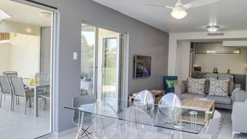 Ein modernes Wohnzimmer mit einem Glastisch, transparenten Stühlen, einem grauen Sofa und einem Deckenventilator.
