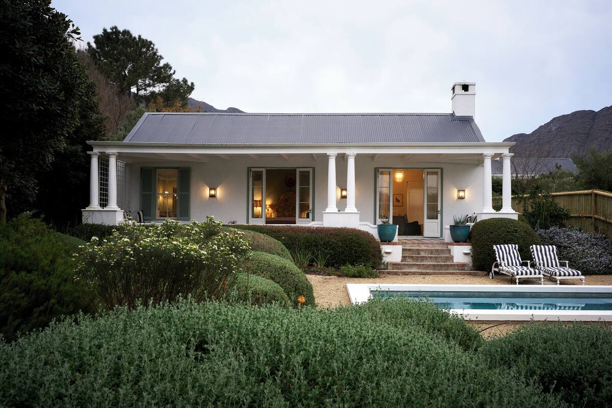 A two-story house with a covered porch, a swimming pool, and a mountainous backdrop.