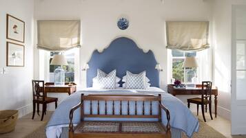 A bedroom with a large bed, two bedside tables, a wooden bench, and a desk with chairs.