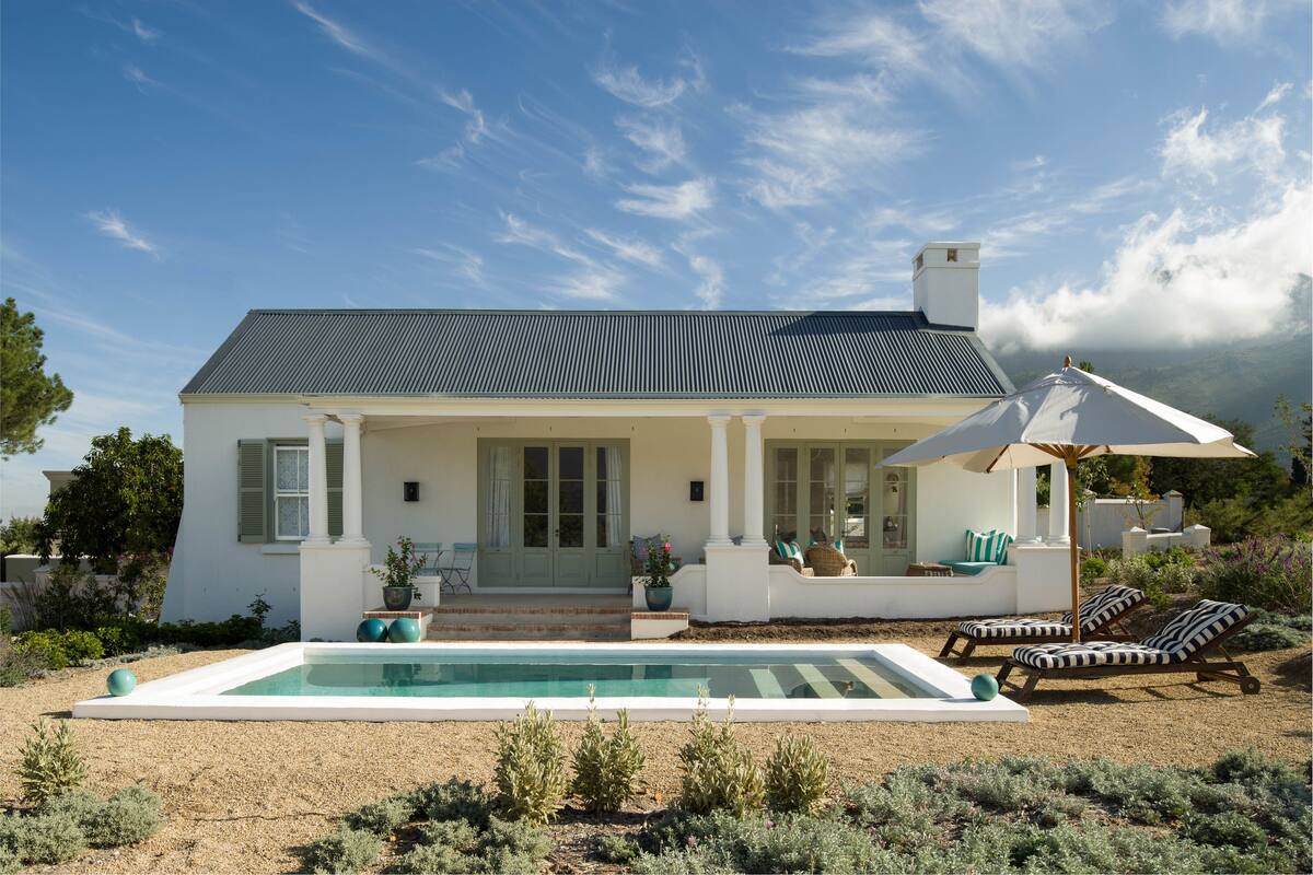 A white house with a pool, outdoor seating, and a view of the mountains.