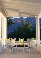 A covered patio with two wicker chairs and a bench, overlooking a mountainous landscape.