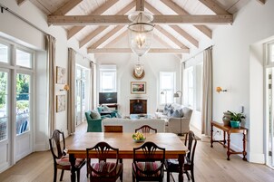 A spacious living room with a wooden dining table, comfortable seating, and large windows.