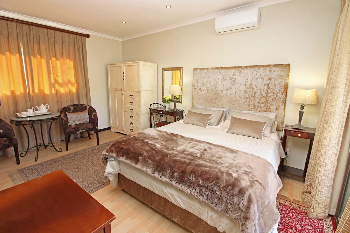 A hotel room with a large bed, a desk, a chair, a wardrobe, and a lamp.