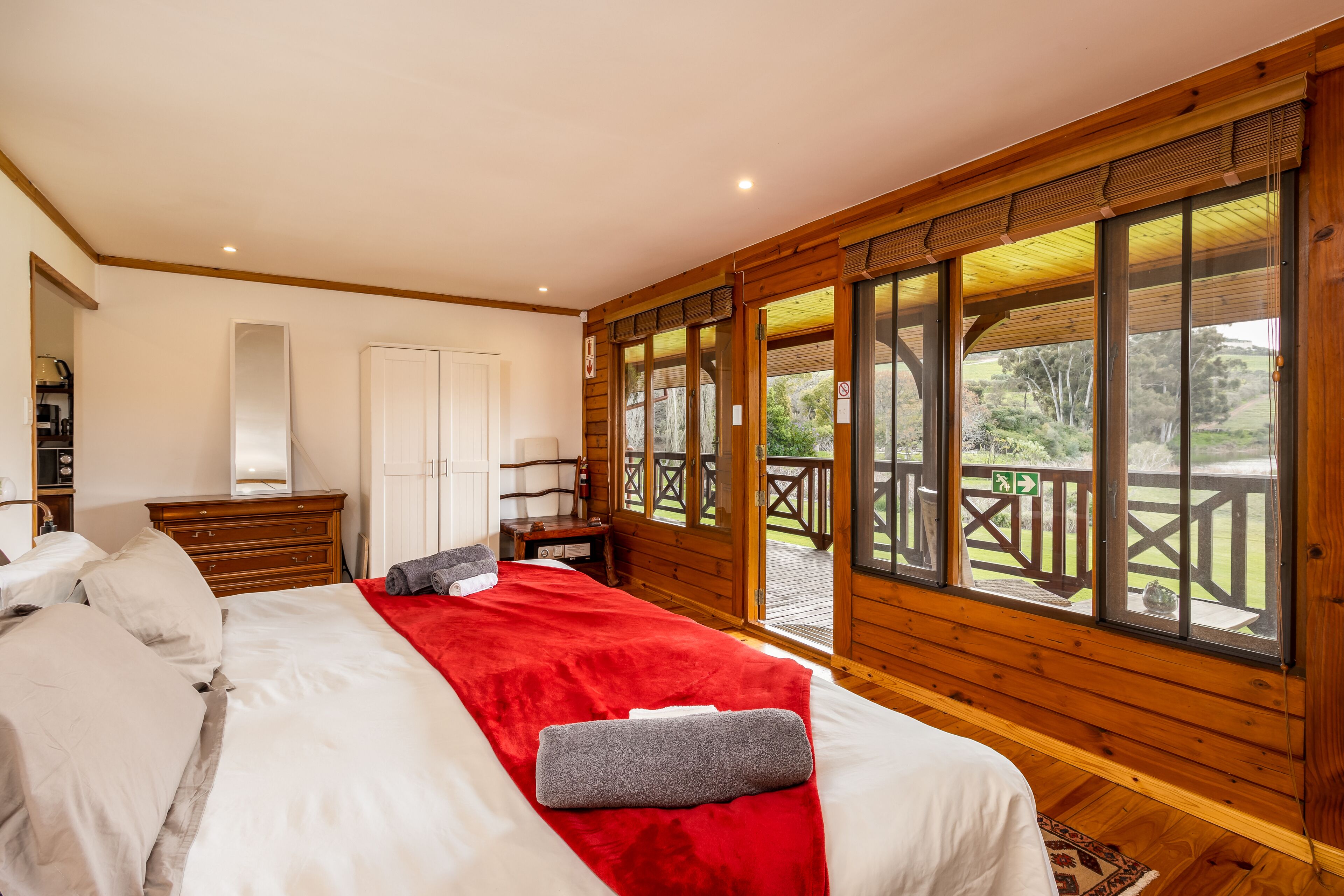 A bedroom with a large bed, wooden walls, and a balcony with a view of the outdoors.