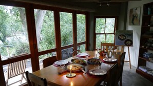 A dining table set with plates, glasses, and a candle, with large windows offering a view of greenery outside. - High Hopes (Greyton)