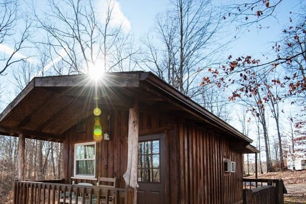 Une cabane en bois dotée d’une véranda et d’une fenêtre, entourée d’arbres.