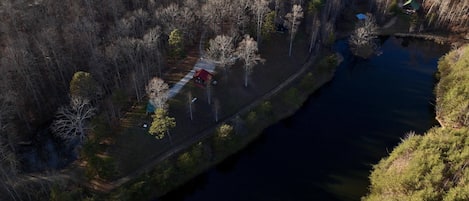 An aerial view of a lakeside property with a red cabin, a dock, and a small boat.