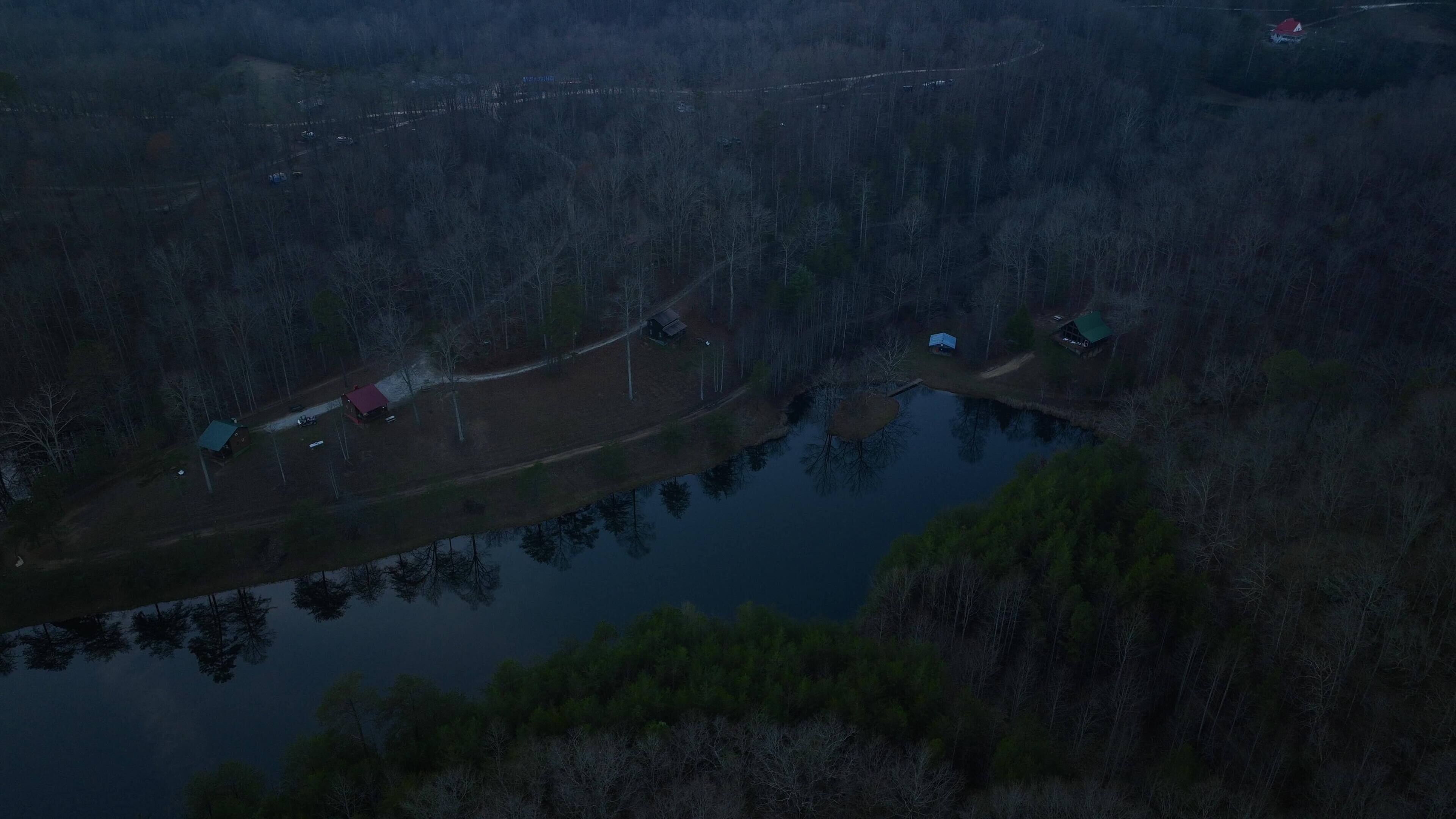 An aerial view of a forested area with a small lake, several cabins, and a road.