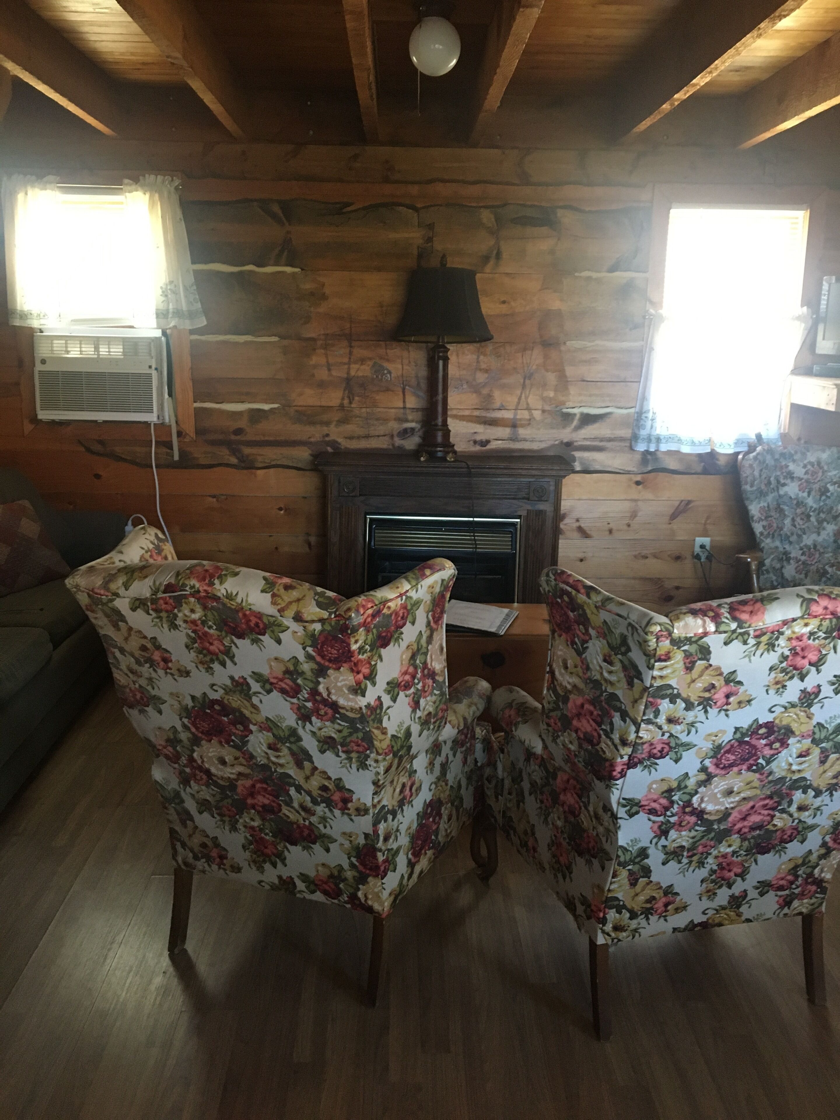 A cozy cabin interior with wooden walls, a fireplace, and floral-patterned chairs.