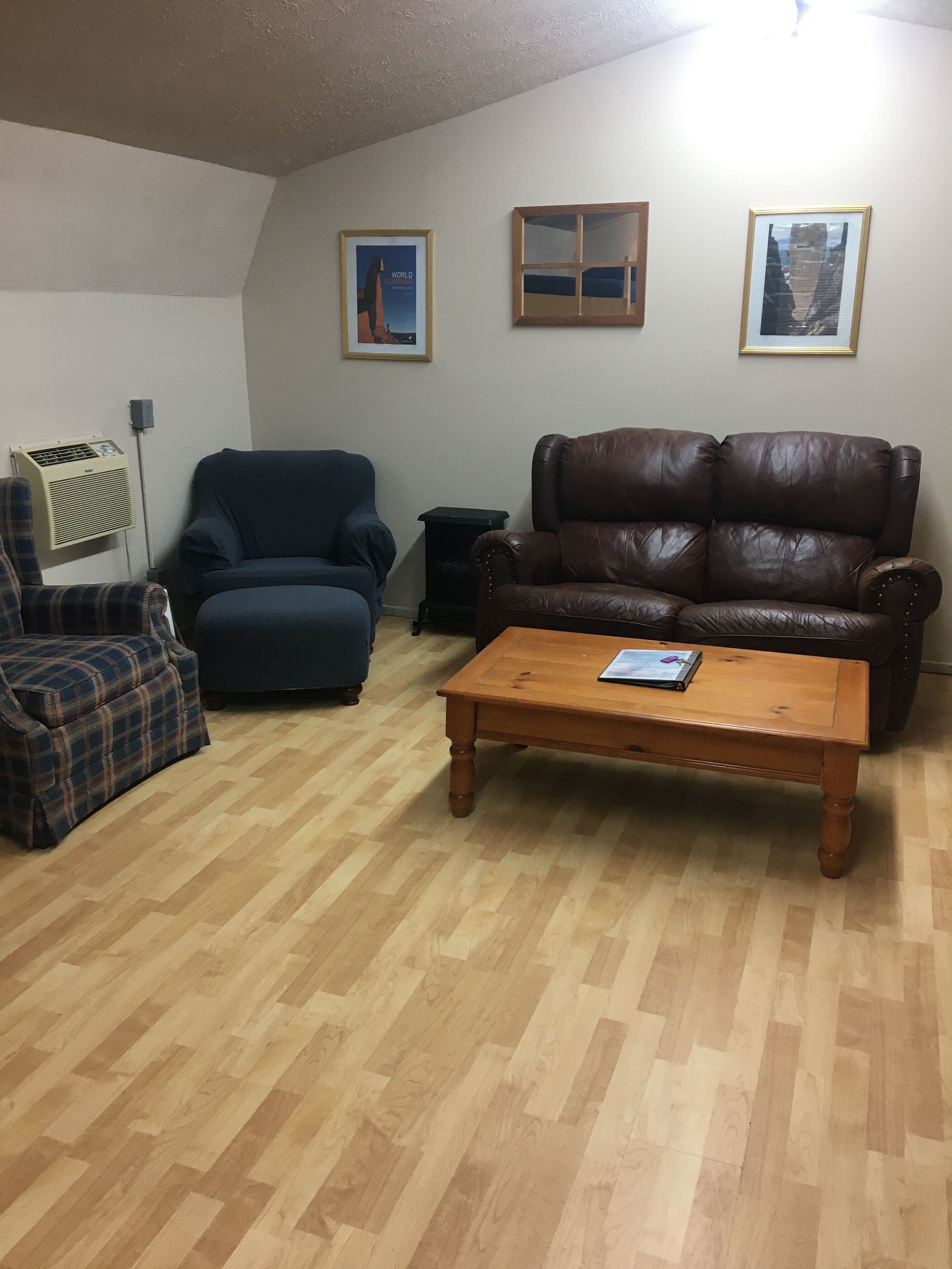 A living room with a brown leather sofa, a blue armchair, a plaid sofa, a wooden coffee table, and two framed pictures on the wall.