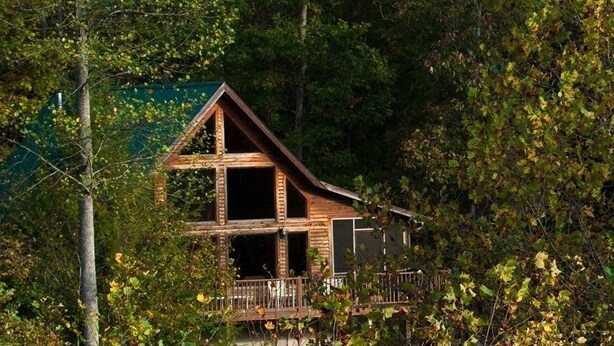 Una cabaña con fachada de madera, un balcón y rodeada de un bosque denso.