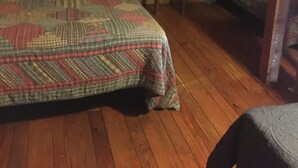 Un dormitorio acogedor en el ático, con techo inclinado de madera, una cama con colcha estampada, una mesita con lámpara y una estantería con calefactor.