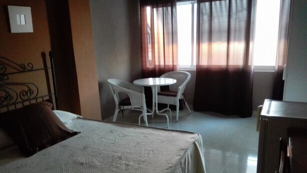 Une chambre d’hôtel avec un lit, une petite table et deux chaises, une fenêtre avec des rideaux et une armoire.