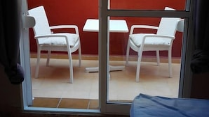 Une pièce dotée d’une porte-fenêtre coulissante donnant sur un espace extérieur aménagé avec deux fauteuils en osier blancs et une petite table.