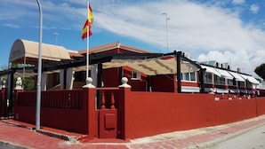 Un bâtiment rouge avec un drapeau, un espace abrité et une enseigne sur laquelle on peut lire « HOSTAL ».