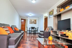 A modern living room with a sofa set, a glass coffee table, a flat-screen TV, and a dining area with chairs and a table.