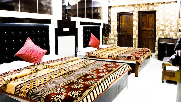 A hotel room with two beds, each with a patterned bedspread, a red pillow, and a headboard. There is a wooden door and a small table in the room. - Hotel Suntejpaza (Nainital)