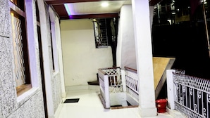 A corridor with a white tiled floor, a white bench, and a metal railing. - Hotel Suntejpaza (Nainital)