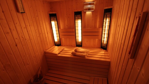 Una sauna de madera con bancos y un asiento, una toalla en uno de los bancos, y un perchero.