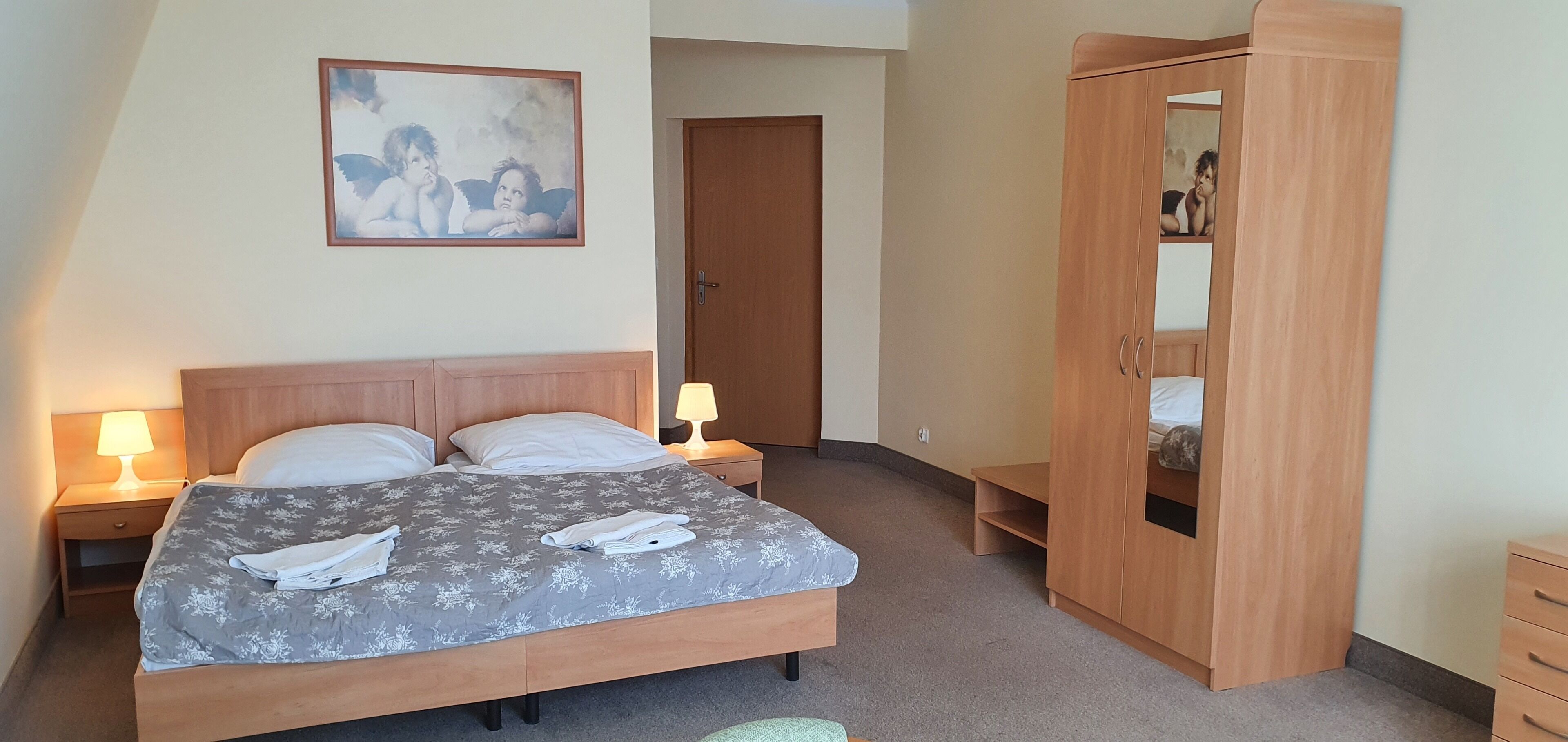 A hotel room with a bed, two bedside tables with lamps, a wooden wardrobe, and a framed picture on the wall.