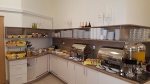 Montaje de bufé con diversos alimentos, utensilios de servicio y dispensadores de bebidas.